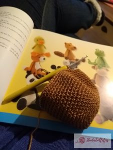 Foto van overzicht van knuffels in het boek met daarvoor een haakwerkje met haaknaald.